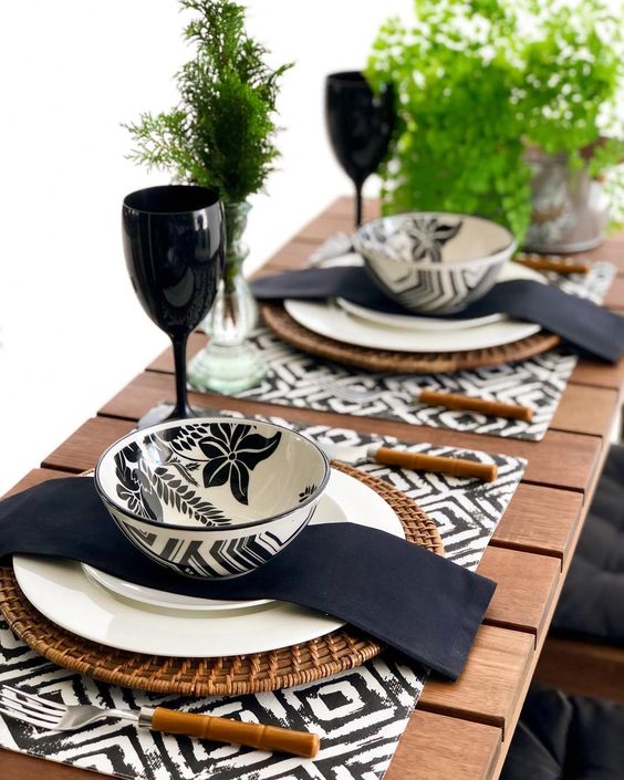 An eye catchy black and white Thanksgiving tablescape with printed placemats, printed bowls, black napkins, greenery and black glasses
