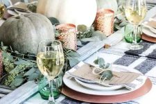 greenery, green and white pumpkins, candleholders, green glasses and greenery on the place settings for Thanksgiving