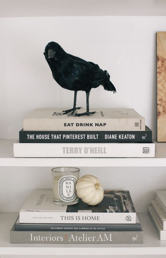 minimalist Halloween decor with a blackbird, a white pumpkin and a candle plus black and white books is awesome