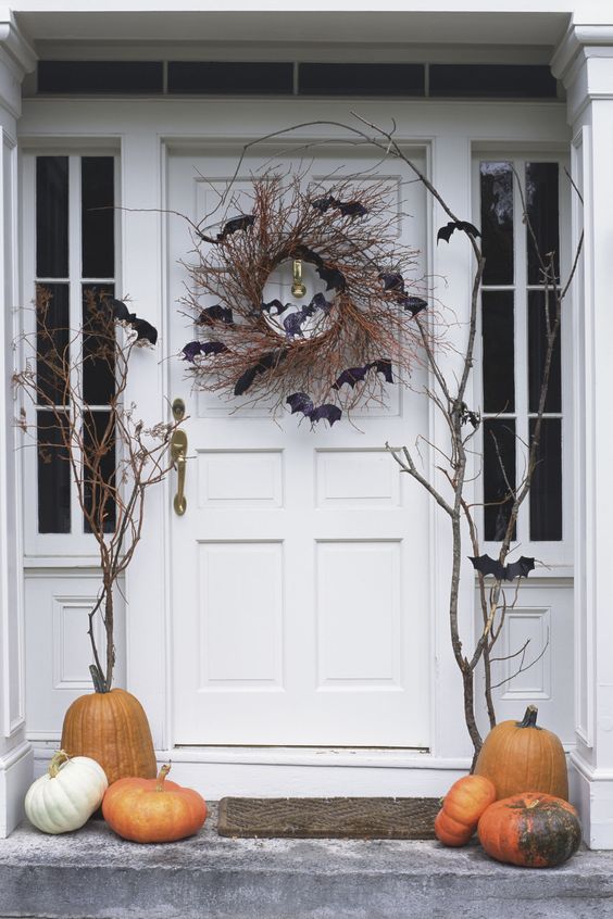 rustic Halloween porch styling with branches, pumpkins, a vine wreath with bats is a simple and cool idea
