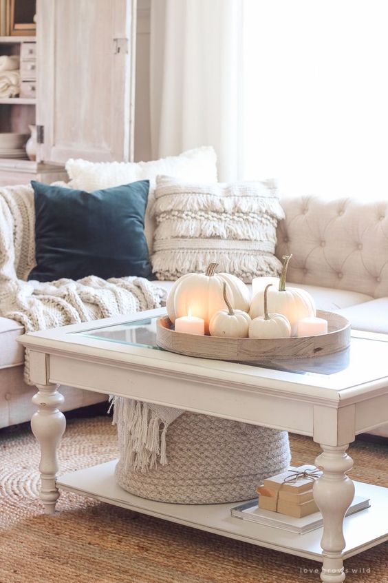 simple and cool Thanksgiving decor with a wooden tray, white candles and pumpkins, a basket with neutral blankets