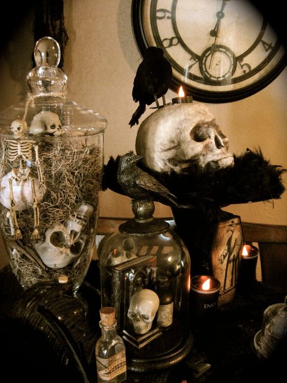 vintage Halloween decor with jars and cloches with skulls and skeletons, a skull on a stand, some candles and a blackbird