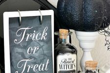 vintage Halloween decor with a sign, vintage potion bottles, white stands with black glitter pumpkins is a chic and bold idea