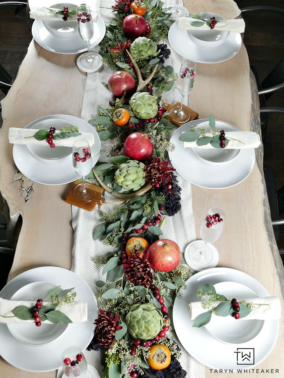 a beautiful natural Thanksgiving tablescape with a greenery runner, bold blooms, pomegranates, persimmons, artichokes and antlers