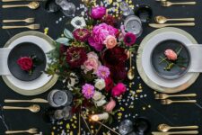 a black and gold NYE table setting with gold chargers and cutlery, gold candleholders, bright blooms and gold and silver sequins on the table