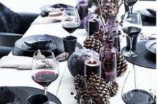 a black and purple New Year’s table setting with oversized pinecones, purple candles and black chargers and plates