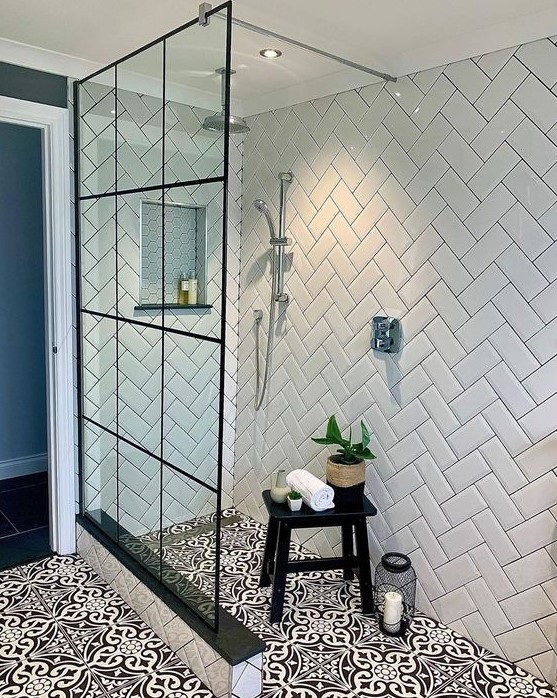 a black and white bathroom with white chevron tiles on the walls, black and white Moroccan tiles on the floor and a glass shower wall