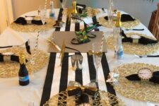 a black, gold and white NYE tablescape with a striped runner, gold placemats, black napkins and clocks, greenery and mini champagne bottles