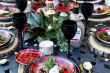 a bold Christmas tablescape with plaid plates and red candles, evergreens and magnolia leaves plus black napkins and glasses