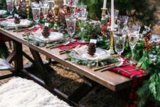 a bold outdoor Christmas tablescape with an evergreen and red plaid runner, evergreen placemats, tall and thin candles, berries on the table and some pinecones
