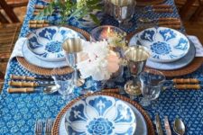 a bright Thanksgiving table setting with printed plates, a printed tablecloth, woven elements and neutral blooms