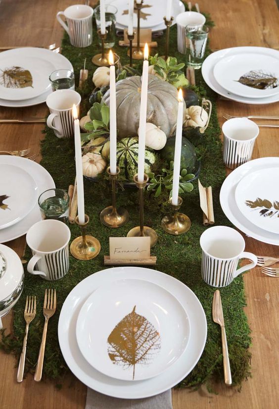 a chic Thanksgiving tablescape with a moss runner, pumpkins, greenery, candles and and gold leaves