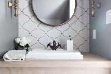 a chic and refined bathroom in neutrals, with grey walls and a white arabesque tile accent wall, a round mirror, chic sconces is amazing