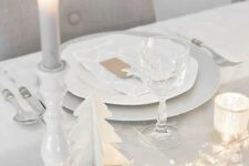 a clean white tablescape with a dove grey table runner, LEDs, stars, candles and wooden fir trees