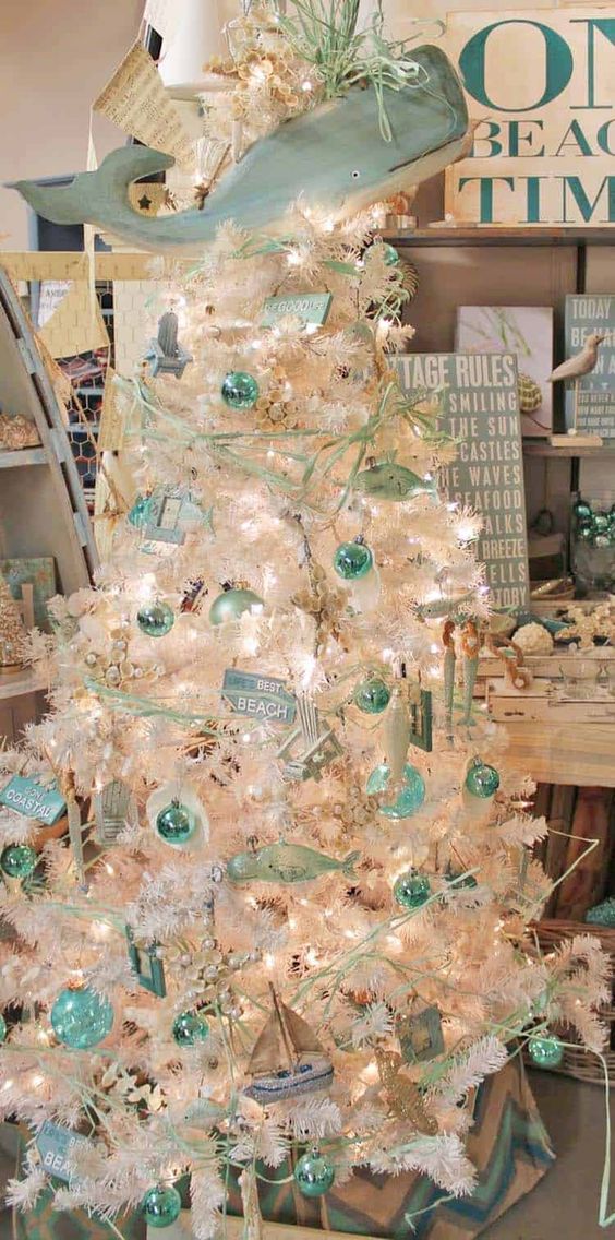a coastal chic Christmas tree in white, with aqua and mint ornaments, branches, signs, boats and a large whale as a tree topper