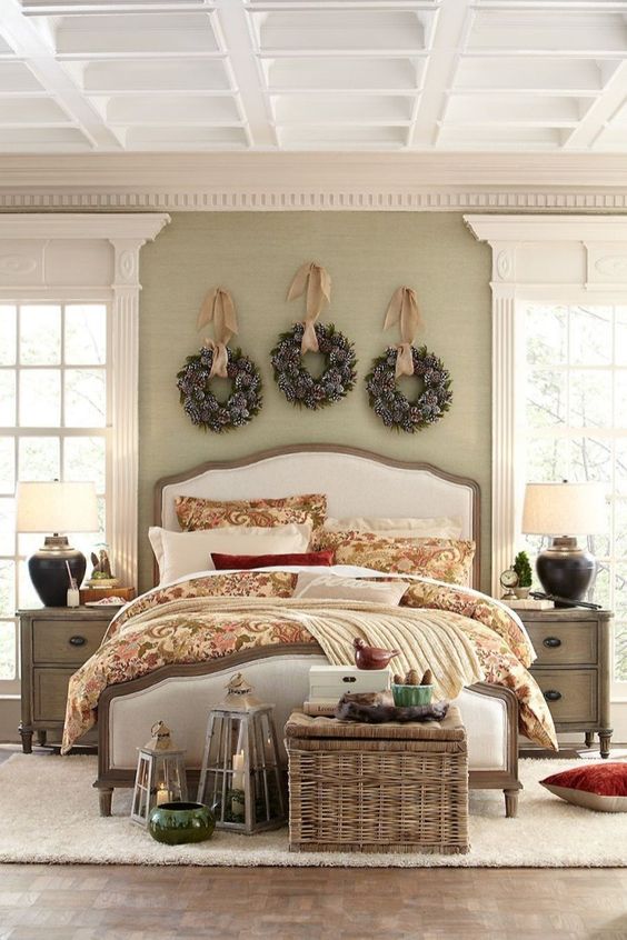 a cozy Christmas bedroom with snowy evergreen wreaths over the bed, candle lanterns, a basket chest with storage
