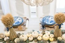 a cozy Thanksgiving table setting with woven placemats, blue plates with birds, wheat with blue ties and neutral pumpkins