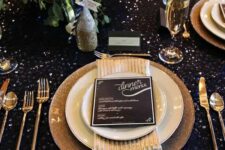 a dark sequin tablecloth, gold glitter chargers, gold cutlery and a lush greenery and bloom centerpiece