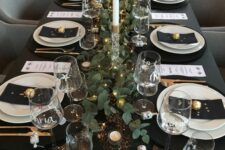 a dreamy NYE tablescape in black, with black linens, white porcelain, a greenery runner with LED lights, tall and thin candles