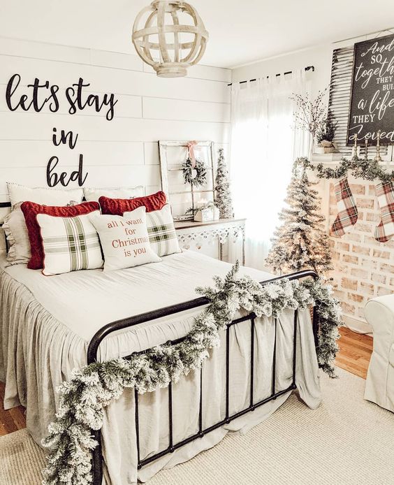 a farmhouse chic bedroom with snowy garlands, mini trees, a sign, plaid bedding and a wreath for a Christmas feel int the space