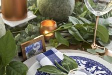 a greenery and copper tablescape with blue and white plates and napkins plus cards make up a gorgeous setting for Thanksgiving