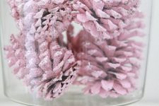 a large glass bowl with pastel pink pinecones is a pretty modern decoration for the holidays and it will add a soft touch to the spac