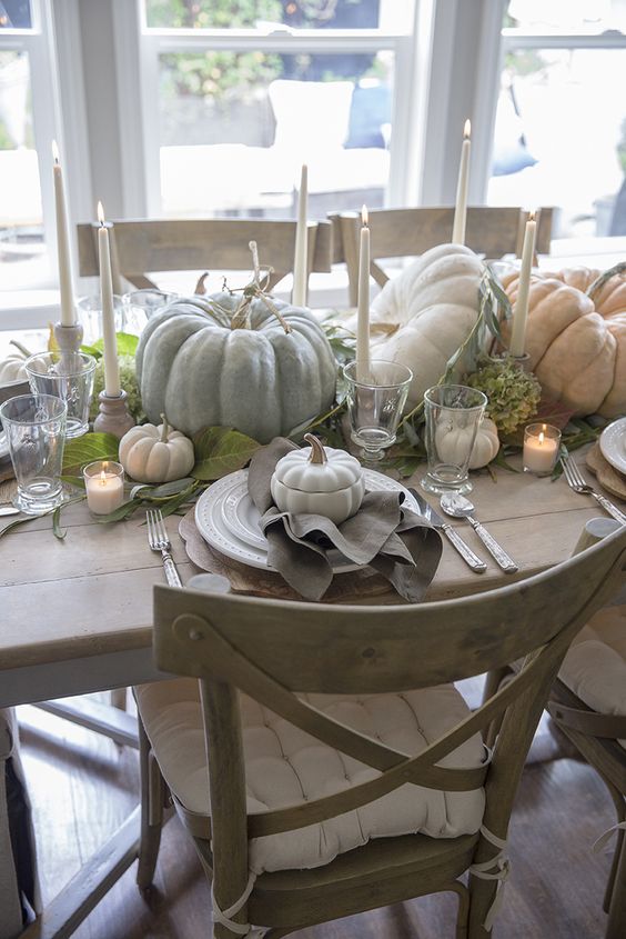 a lovely natural Thanksgiving tablescape with neutral heirloom pumpkins, tall candles, greenery and neutral linens