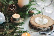 a lovely outdoor Christmas tablescape with neutral linens, an evergreen table runner, snowy pinecones, nuts and candles