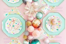 a lovely pastel Christmas tablescape with a pink tablecloth, mint grene hex plates, a pastel ornament garland and bright plates