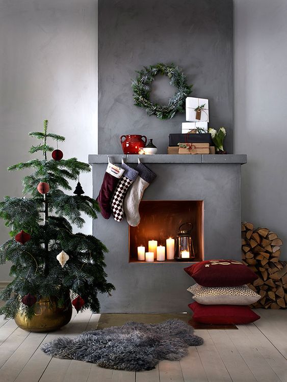 a mini Christmas tree with bright ornaments, stacked pillows, bright stockings, a flocked greenery wreath and firewood