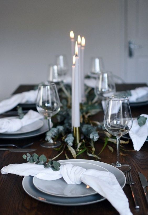 a minimalist Christmas table with eucalyptus, white napkins and grey plates plus candles