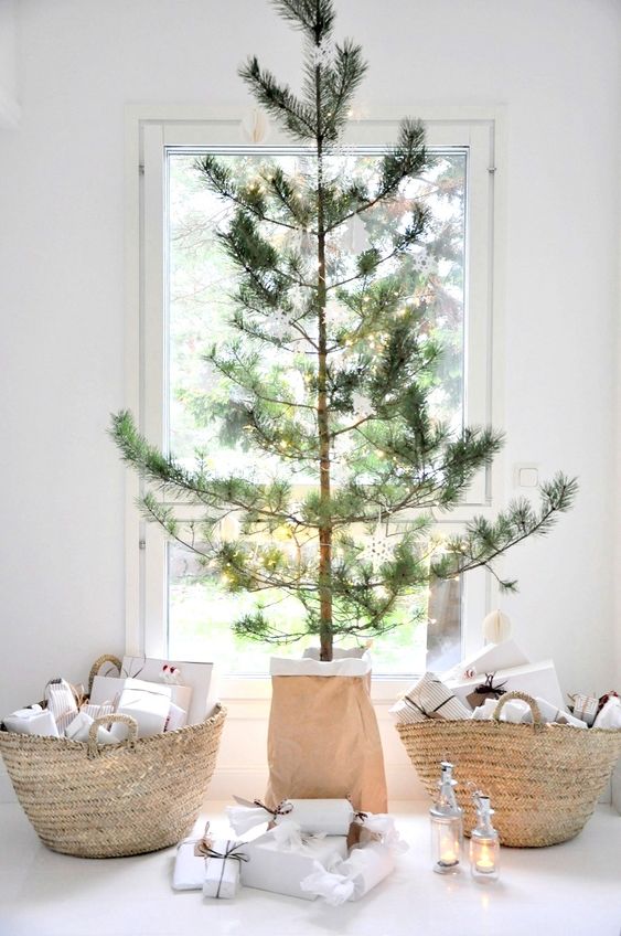 a minimalist Christmas tree with lights only, basket bags filled with gifts and some candle lanterns under the tree