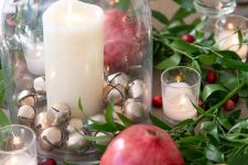 a natural Christmas centerpiece of greenery, berries, pomegranates, candles and a glass jar with mini bells and candles