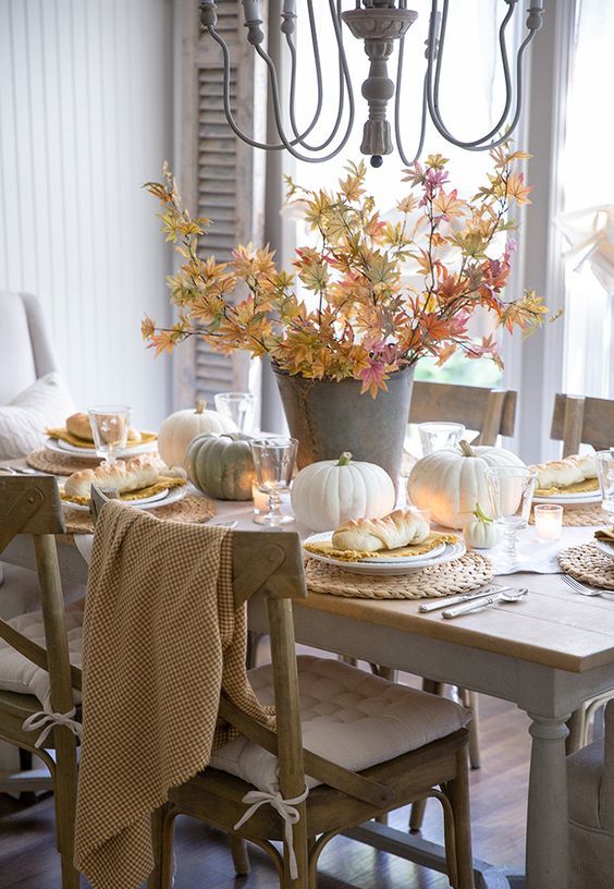 a natural Thanksgiving tablescape with neutral pumpkins, fall leaves, candles and woven chargers is a lovely idea