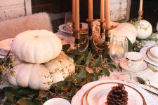 a natural Thanksgiving tablescape with white pumpkins, tall candles and a greenery runner plus pinecones is chic
