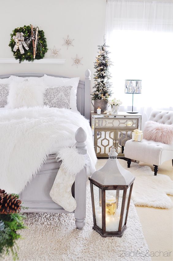 a neutral Christmas bedroom with a snowy mini tree, an evergren wreath with skis, a stocking, an oversized lantern and a faux fur blanket