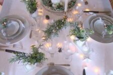 a neutral holiday table setting with lots of fresh greenery, ornaments, lights and candles