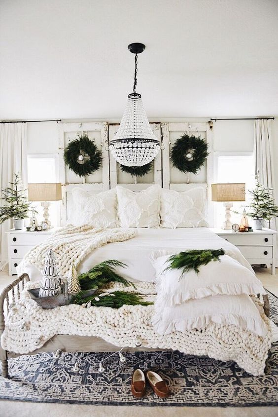 a neutral shabby chic Christmas bedroom with evergreen wreaths, garlands, knit blankets and mini Christmas trees