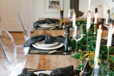 a pretty NYE tablescape with black placemats and printed black napkins, a greenery runner with LEd lights and champagne bottles