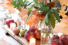 a pretty fall or Thanksgiving centerpiece of apples, fall leaves and candles on a wooden board is lovely