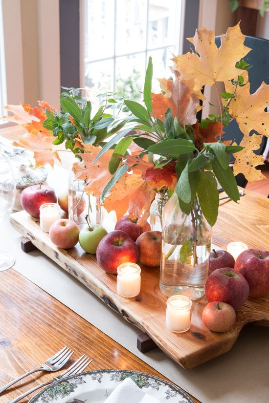 a pretty fall or Thanksgiving centerpiece of apples, fall leaves and candles on a wooden board is lovely