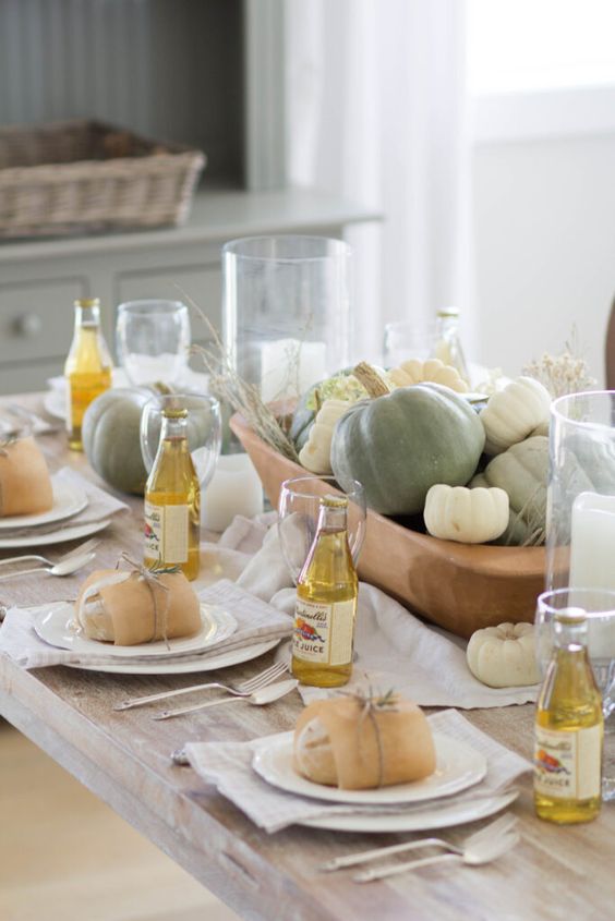 a pretty neutral Thanksgiving tablescape with a bowl filled with pumpkins and more pumpkins around looks chic