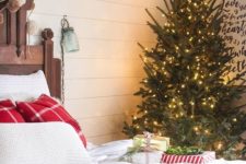 a red and white bedding set, a Christmas tree with lots of lights, pompom garlands and gift boxes right on the bed