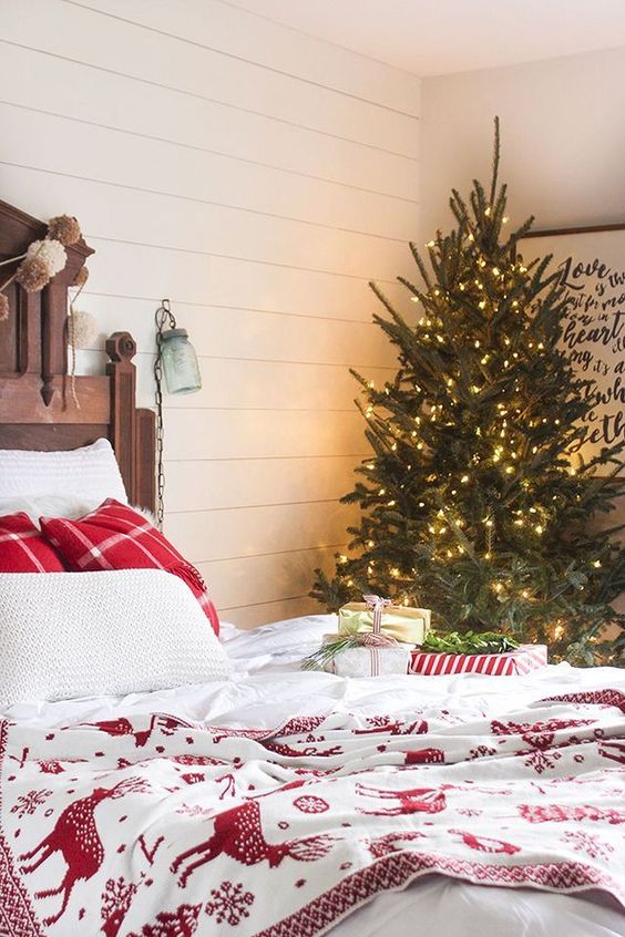 a red and white bedding set, a Christmas tree with lots of lights, pompom garlands and gift boxes right on the bed
