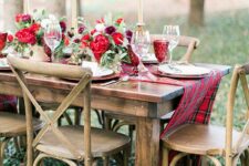 a refined Christmas tablescape with a plaid table runner, bold red blooms and red glasses, tall and thin candles and white porcelain