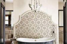 a refined bathroom with geo and Moroccan tiles, a metal clad bathtub, a mirrored chandelier and some neutral furniture