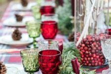 a rustic Christmas tablescape with an evergreen runner, a vase with cranberries and whitewashed branches, red and green glasses