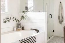 a serene farmhouse bathroom with white planked walls, grey and white Moroccan tiles, a bathtub covered with white panels, a woven lamp