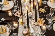 a shiny glam NYE tablescape with a silver sequin runner, white porcelain, black candles, gold cutlery and clocks and disco balls