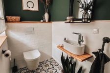 a small and chic powder room with green walls and white tiles, pretty Moroccan tiles on the floor, white applainces and some potted plants